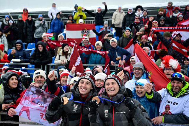 Bronze medallists Austria's Johannes Lamparter (L) and Stefan Rettenegger celebrate with Austrian fans following the nordic combined team sprint large hill event at Tesero Cross Country Stadium at Lago di Tesero (Val di Fiemme) during the Milano Cortina 2026 Winter Olympic Games on February 19, 2026.  (Photo by Tobias SCHWARZ / AFP)