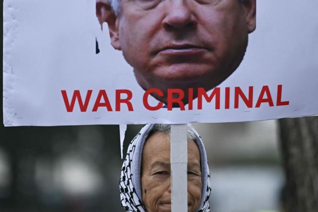 A woman holds a picture of Israel's Prime Minister Benjamin Netanyahu reading "war criminal" as demonstrators protest outside of the US Institute of Peace as President Donald Trump hosts the inaugural meeting of the "Board of Peace" at the in Washington, DC, on February 19, 2026. President Trump on Thursday gathers allies to inaugurate the "Board of Peace," his new institution focused on progress on Gaza but whose ambitions reach much further. Around two dozen world leaders or other senior officials have come to Washington for the meeting -- including several of Trump's authoritarian-leaning friends and virtually none of the European democrats that traditionally sign on to US initiatives. (Photo by Brendan SMIALOWSKI / AFP)