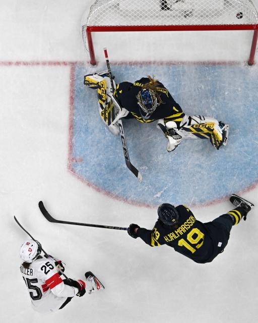Switzerland's #25 Alina Muller (bottom L) scores the decisive 2-1 goal against Sweden's #01 Ebba Svensson Traff (top R) during the women's bronze medal ice hockey match between Switzerland and Sweden at the Milano Santagiulia Ice Hockey Arena during the Milano Cortina 2026 Winter Olympic Games in Milan, on February 19, 2026. (Photo by Alexander NEMENOV / AFP)