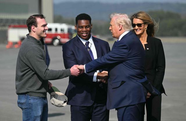 US President Donald Trump shakes hands with University of Georgia football quarterback Gunner Stockton (L) and Herschel Walker (2L), US Ambassador to the Bahamas, after stepping off Air Force One upon arrival at Richard B. Russell Regional Airport in Rome, Georgia, on February 19, 2026. Trump is in northwest Georgia to visit local businesses and give remarks about the economy at a steel factory. (Photo by SAUL LOEB / AFP)
