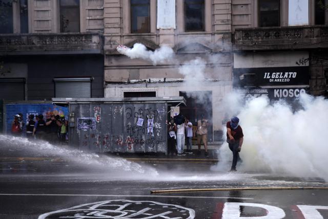 A demonstrator throws back a tear gas canister launched by police as they spray water at protesters outside the Congress building, where Argentina's President Javier Milei's labour reform is being treated, in Buenos Aires on February 19, 2026. Shops and supermarkets closed, public transport was scarce and garbage went uncollected on February 19, 2026 as Argentine workers staged the fourth general strike of President Javier Milei's term, this time to protest labor reforms. (Photo by TOMAS CUESTA / AFP)