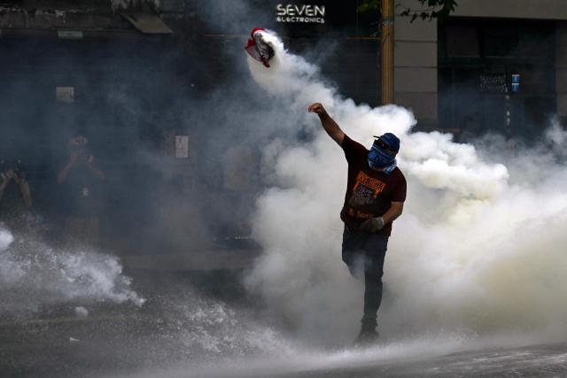 A demonstrator throws back a tear gas canister launched by police during a protest outside the Congress building, where Argentina's President Javier Milei's labour reform is being treated, in Buenos Aires on February 19, 2026. The contested reforms pushed by Argentina's President Javier Milei would make it easier to hire and fire workers in a country where job security is already hard to come by. It would also reduce severance pay, limit the right to strike, increase work hours and restrict holiday provisions. (Photo by Luis ROBAYO / AFP)