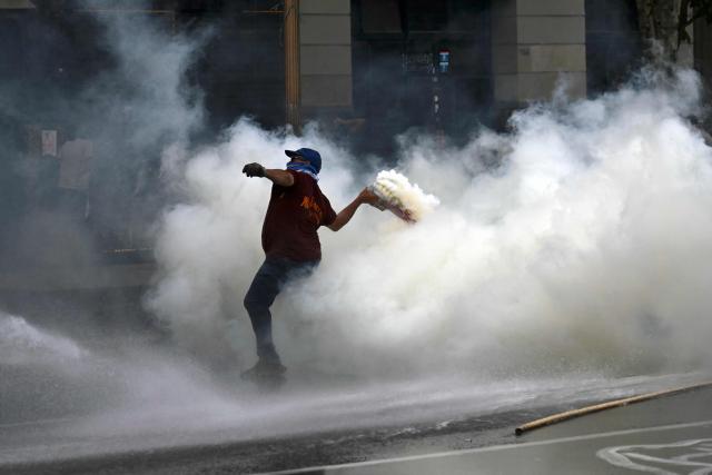 A demonstrator throws back a tear gas canister launched by police during a protest outside the Congress building, where Argentina's President Javier Milei's labour reform is being treated, in Buenos Aires on February 19, 2026. The contested reforms pushed by Argentina's President Javier Milei would make it easier to hire and fire workers in a country where job security is already hard to come by. It would also reduce severance pay, limit the right to strike, increase work hours and restrict holiday provisions. (Photo by Luis ROBAYO / AFP)