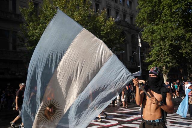 A demonstrator holds an Argentine flag during a protest outside the Congress building, where Argentina's President Javier Milei's labour reform is being treated, in Buenos Aires on February 19, 2026. The contested reforms pushed by Argentina's President Javier Milei would make it easier to hire and fire workers in a country where job security is already hard to come by. It would also reduce severance pay, limit the right to strike, increase work hours and restrict holiday provisions. (Photo by TOMAS CUESTA / AFP)
