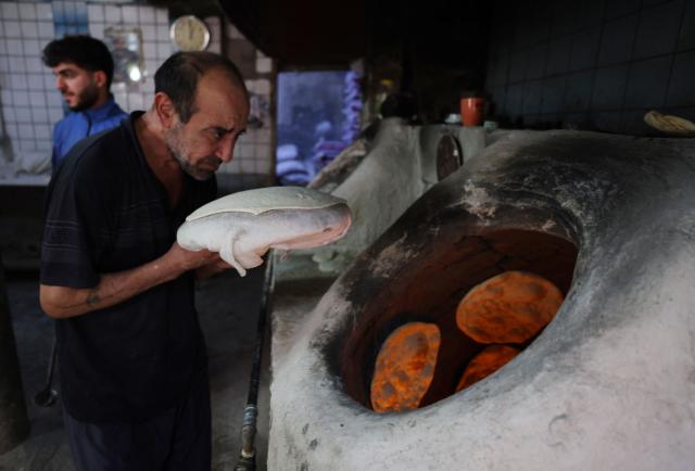 An Iraqi baker places dough inside a stone oven to bake in his bakery during the Muslim holy fasting month of Ramadan in Baghdad on February 19, 2026. Muslims throughout the world are marking the month of Ramadan, the holiest month in the Islamic calendar, during which devotees fast from dawn until dusk. (Photo by AHMAD AL-RUBAYE / AFP)