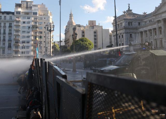 Demonstrators push a fence as a water canon attempts to disperse them during a protest outside the Congress building, where Argentina's President Javier Milei's labour reform is being treated, in Buenos Aires on February 19, 2026. The contested reforms pushed by Argentina's President Javier Milei would make it easier to hire and fire workers in a country where job security is already hard to come by. It would also reduce severance pay, limit the right to strike, increase work hours and restrict holiday provisions. (Photo by TOMAS CUESTA / AFP)