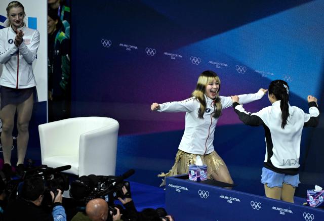 Japan's Ami Nakai (R) reacts in the kiss and cry area next to USA's Alysa Liu (C) as USA's Amber Glenn (L) watches after competing in the figure skating women's single free skating final during the Milano Cortina 2026 Winter Olympic Games at Milano Ice Skating Arena in Milan on February 19, 2026. (Photo by WANG Zhao / AFP)