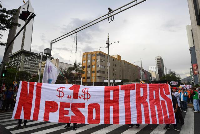 Supporters of Colombian President Gustavo Petro show a banner that reads "Not 1 Peso Back" during a demonstration in Medellin, Colombia on February 19, 2026, to back the vital minimum wage decree, which was provisionally suspended by the Council of State. (Photo by Jaime SALDARRIAGA / AFP)