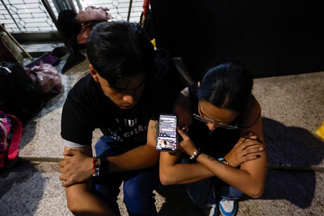 Relatives watch on a cellphone the livestream of Venezuela’s National Assembly President Jorge Rodriguez speaking during a debate on an amnesty bill proposed by Venezuela’s interim president Delcy Rodriguez, outside the El Helicoide building, headquarters of the Bolivarian National Intelligence Service (SEBIN), in Caracas on February 19, 2026. Venezuela's Parliament resumed on February 19 the debate on an amnesty bill that could free hundreds of political prisoners. (Photo by Pedro MATTEY / AFP)