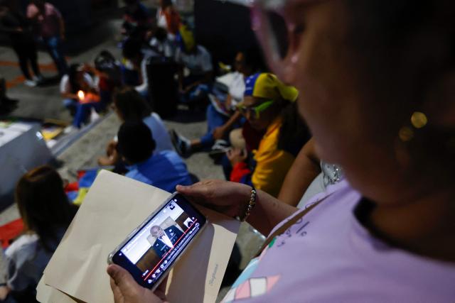 Relatives watch on a cellphone the livestream of Venezuela’s National Assembly President Jorge Rodriguez speaking during a debate on an amnesty bill proposed by Venezuela’s interim president Delcy Rodriguez, outside the El Helicoide building, headquarters of the Bolivarian National Intelligence Service (SEBIN), in Caracas on February 19, 2026. Venezuela's Parliament resumed on February 19 the debate on an amnesty bill that could free hundreds of political prisoners. (Photo by Pedro MATTEY / AFP)