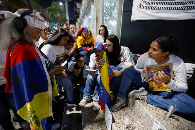 Relatives of political prisoners watch on a cellphone the livestream of Venezuela’s National Assembly President Jorge Rodriguez speaking during a debate on an amnesty bill proposed by Venezuela’s interim president Delcy Rodriguez, outside the El Helicoide building, headquarters of the Bolivarian National Intelligence Service (SEBIN), in Caracas on February 19, 2026. Venezuela's Parliament resumed on February 19 the debate on an amnesty bill that could free hundreds of political prisoners. (Photo by Pedro MATTEY / AFP)