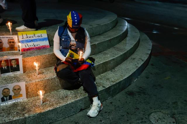 A relative of political prisoner watch on a cellphone the livestream of Venezuela’s National Assembly President Jorge Rodriguez speaking during a debate on an amnesty bill proposed by Venezuela’s interim president Delcy Rodriguez, outside the El Helicoide building, headquarters of the Bolivarian National Intelligence Service (SEBIN), in Caracas on February 19, 2026. Venezuela's Parliament resumed on February 19 the debate on an amnesty bill that could free hundreds of political prisoners. (Photo by Pedro MATTEY / AFP)