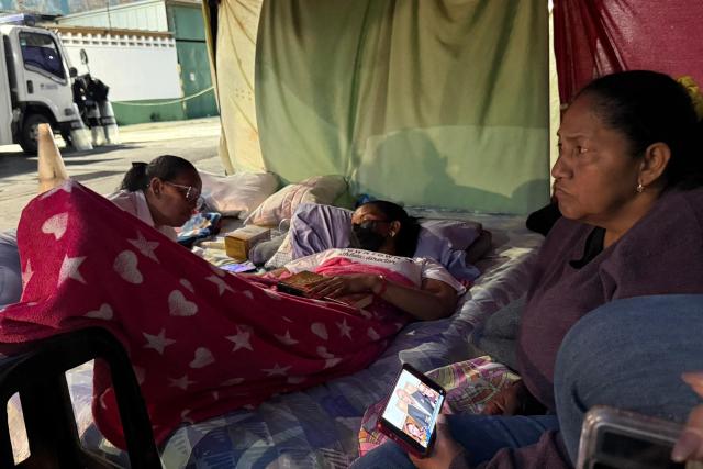 Relatives of political prisoners on hunger strike watch on a cellphone the livestream of Venezuela's National Assembly debate, as lawmakers discuss an amnesty bill proposed by interim president Delcy Rodriguez, outside the Bolivarian National Police (PNB) Zona 7 prison in Caracas on February 19, 2026. Venezuela's Parliament unanimously approved on February 19 a historic amnesty law that is expected to lead to the release of hundreds of political prisoners after 27 years of Chavismo. (Photo by Yorman MALDONADO / AFP)