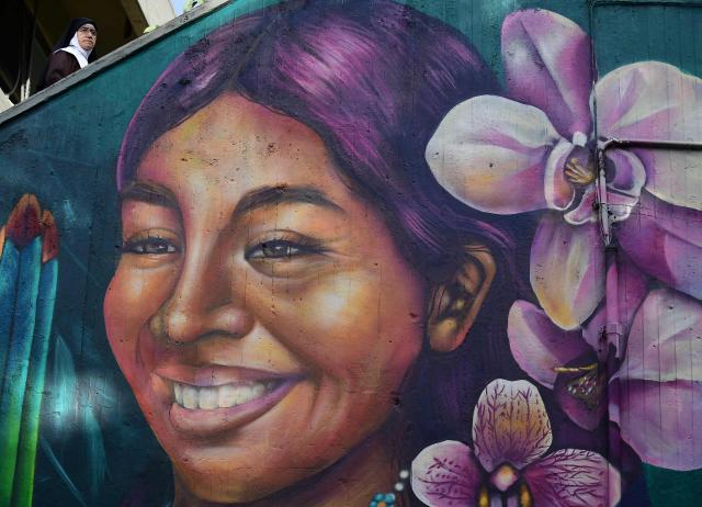 A nun walks past a mural at El Pueblito Paisa, a scale replica of a traditional 20th-century Antioquian village, located atop Nutibara Hill in Medellin, Colombia on February 18, 2026. (Photo by JAIME SALDARRIAGA / AFP)