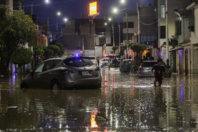 A man walks next to a car in the middle of a flood caused by heavy rains in the Yanahuara district of Arequipa, southern Peru, on February 19, 2026. (Photo by Juan Santy / AFP)