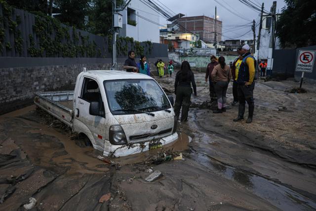 People look on next to a car in the mud caused by heavy rains in the Yanahuara district of Arequipa, southern Peru, on February 19, 2026. (Photo by Juan Santy / AFP)
