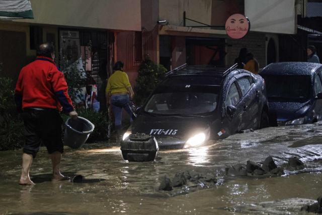 A man walks without shoes next to a car in the mud caused by heavy rains in the Yanahuara district of Arequipa, southern Peru, on February 19, 2026. (Photo by Juan Santy / AFP)