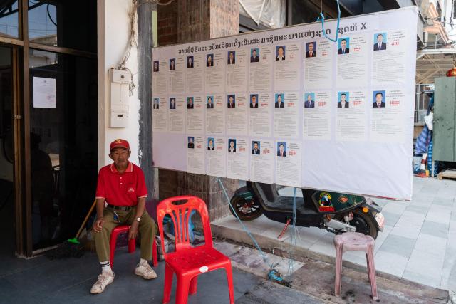 A man sits outside a village office next to a board displaying the names and photos of candidates ahead of the election in Vientiane on February 19, 2026. The February 22 election will see 243 candidates contest 175 seats after being pre-selected by the ruling communist party. The Southeast Asian nation has no opposition parties, no fully independent news outlets, and the ruling Lao People's Revolutionary Party has held power for more than 50 years. (Photo by AFP)