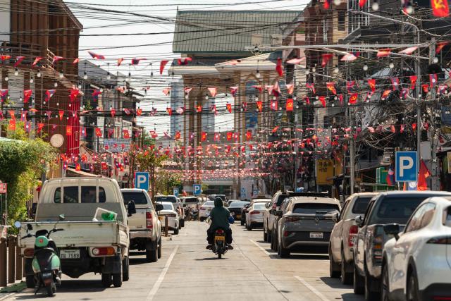 A motorist rides past Laos national flags and Lao People's Revolutionary Party flags displayed ahead of the election in downtown Vientiane on February 19, 2026. The February 22 election will see 243 candidates contest 175 seats after being pre-selected by the ruling communist party. The Southeast Asian nation has no opposition parties, no fully independent news outlets, and the ruling Lao People's Revolutionary Party has held power for more than 50 years. (Photo by AFP)
