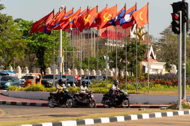 Motorists drive past Laos national flags and Lao People's Revolutionary Party flags ahead of the election in Vientiane on February 19, 2026. The February 22 election will see 243 candidates contest 175 seats after being pre-selected by the ruling communist party. The Southeast Asian nation has no opposition parties, no fully independent news outlets, and the ruling Lao People's Revolutionary Party has held power for more than 50 years. (Photo by AFP)