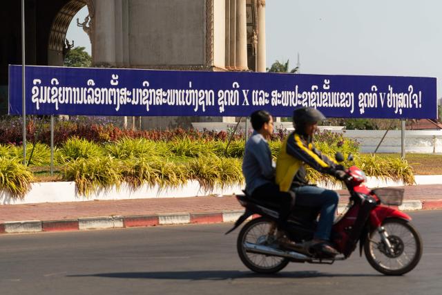 A motorist drives past a banner that translates as "Congratulations to the election of representatives to the 10th National Assembly of 5th Members of the Provincial Peoples Councils" displayed ahead of the election next to Patuxai, also known as the Victory Monument, in Vientiane on February 19, 2026. The February 22 election will see 243 candidates contest 175 seats after being pre-selected by the ruling communist party. The Southeast Asian nation has no opposition parties, no fully independent news outlets, and the ruling Lao People's Revolutionary Party has held power for more than 50 years. (Photo by AFP)