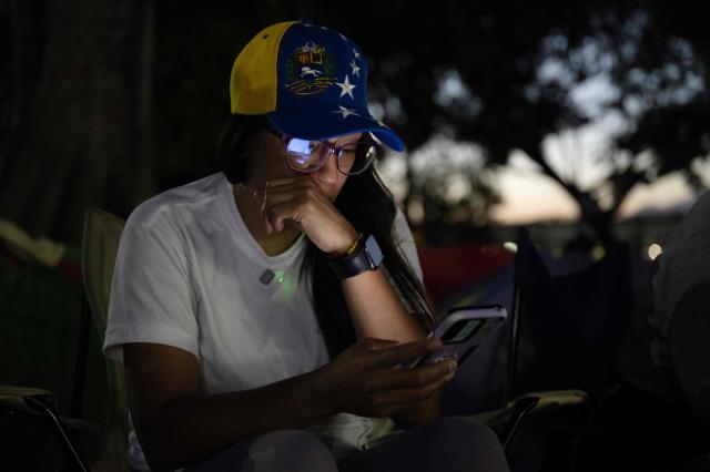 TOPSHOT - A relative of political prisoners watches on a cellphone the livestream of Venezuela’s National Assembly President Jorge Rodriguez speaking during a debate on an amnesty bill proposed by Venezuela’s interim president Delcy Rodriguez, outside El Rodeo I prison in Guatire, Miranda state, Venezuela, on February 20, 2026. Venezuela's Parliament unanimously approved on February 19 a historic amnesty law that is expected to lead to the release of hundreds of political prisoners after 27 years of Chavismo. (Photo by Pedro MATTEY / AFP)