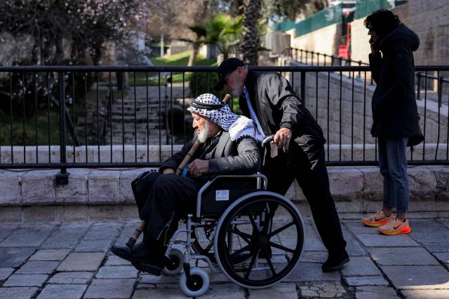 A man pushes a wheelchair-bound elder outside the Damascus Gate of the old city of Jerusalem on the first Friday of the Muslim holy month of Ramadan on February 20, 2026. (Photo by Ilia YEFIMOVICH / AFP)