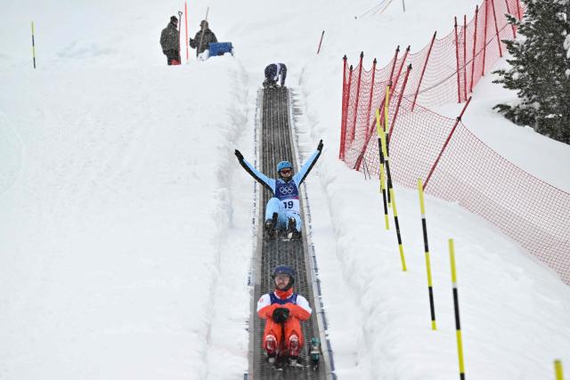 competitors ascend the slope on a conveyor belt, commonly referred to as the "Magic Carpet", before the freestyle skiing men's aerials qualification 2 during the Milano Cortina 2026 Winter Olympic Games at Livigno Aerials & Moguls Park, in Livigno (Valtellina), on February 20, 2026. (Photo by Jeff PACHOUD / AFP)