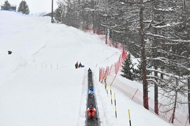 Competitors ascend the slope on a conveyor belt, commonly referred to as the "Magic Carpet", before the freestyle skiing men's aerials qualification 2 during the Milano Cortina 2026 Winter Olympic Games at Livigno Aerials & Moguls Park, in Livigno (Valtellina), on February 20, 2026. (Photo by Jeff PACHOUD / AFP)