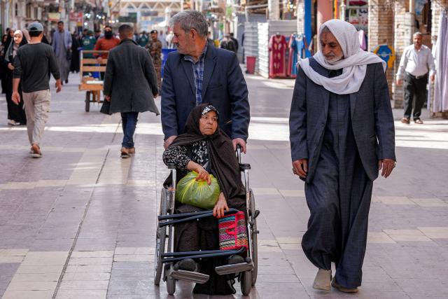 A man pushes a wheelchair-bound disabled woman in Iraq's central holy city of Najaf on February 19, 2026 during the Muslim fasting month of Ramadan. (Photo by Qassem al-KAABI / AFP)