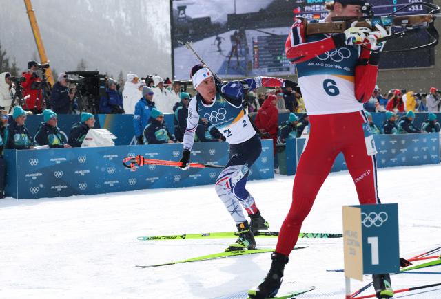 France's Quentin Fillon Maillet (L) leaves the shooting range as Norway's Sturla Holm Laegreid keeps on shooting during the men's biathlon 15km mass start event during the Milano Cortina 2026 Winter Olympic Games at the Anterselva Biathlon Arena (Sudtirol Arena) in Anterselva (Val Pusteria) on February 20, 2026. (Photo by Odd ANDERSEN / AFP)