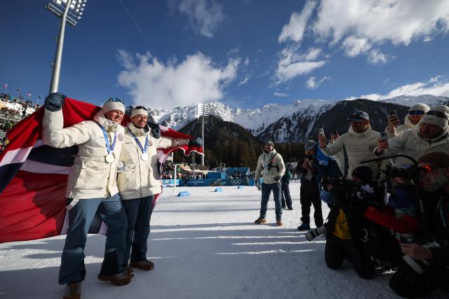 Gold medallist Norway's Johannes Dale-Skjevdal (L) and silver medallist Norway's Sturla Holm Laegreid celebrate with Norway's flag after the podium ceremony of the men's biathlon 15km mass start event during the Milano Cortina 2026 Winter Olympic Games at the Anterselva Biathlon Arena (Sudtirol Arena) in Anterselva (Val Pusteria) on February 20, 2026. (Photo by Franck FIFE / AFP)
