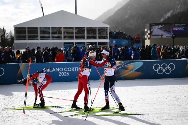 Gold medallist Norway's Johannes Dale-Skjevdal (C) and bronze medallist France's Quentin Fillon Maillet congratulate each other as silver medallist Norway's Sturla Holm Laegreid (L) unlocks his skis after completing the men's biathlon 15km mass start event during the Milano Cortina 2026 Winter Olympic Games at the Anterselva Biathlon Arena (Sudtirol Arena) in Anterselva (Val Pusteria) on February 20, 2026. (Photo by Marco BERTORELLO / AFP)