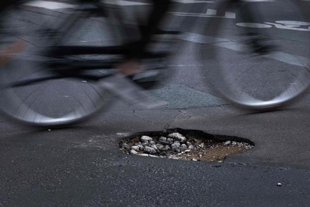 A cyclist rides past a pothole on a cycle path in central Paris on February 20, 2026. (Photo by JOEL SAGET / AFP)