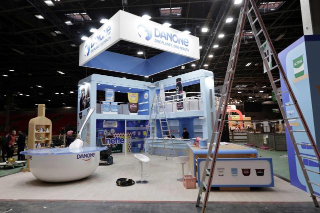 Workers set up the stand of French dairy group Danone before the opening of the 2026 edition of the International Agricultural Show (Salon de l'Agriculture) at Paris Expo Porte de Versailles in Paris on February 20, 2026. Cattle breed selection organisations decided not to enter any cattle in the general agricultural competition at this show and refused to allow any cows to be present, including Biguine, due to the lumpy skin epizootic disease (dermatose nodulaire contagieuse). (Photo by STEPHANE DE SAKUTIN / AFP)