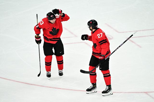 Canada's #27 Shea Theodore (R) celebrates with  Canada's #63 Brad Marchand after scoring his team's second goal during the men's play-off semi-final ice hockey match between Canada and Finland at the Milano Santagiulia Ice Hockey Arena during the Milano Cortina 2026 Winter Olympic Games in Milan, on February 20, 2026. (Photo by JULIEN DE ROSA / AFP)