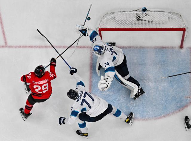 Finland's #74 Juuse Saros (R) saves the puck from a shot at goal by Canada's #29 Nathan Mackinnon during the men's play-off semi-final ice hockey match between Canada and Finland at the Milano Santagiulia Ice Hockey Arena during the Milano Cortina 2026 Winter Olympic Games in Milan, on February 20, 2026. (Photo by JULIEN DE ROSA / AFP)