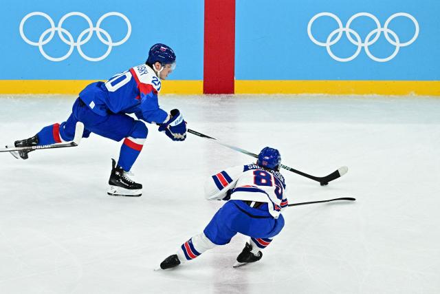 Slovakia's #20 Juraj Slafkovsky (L) and USA's #85 Jake Sanderson vie for the puck during the men's play-off semi-final ice hockey match between USA and Slovakia at the Milano Santagiulia Ice Hockey Arena during the Milano Cortina 2026 Winter Olympic Games in Milan, on February 20, 2026. (Photo by JULIEN DE ROSA / AFP)
