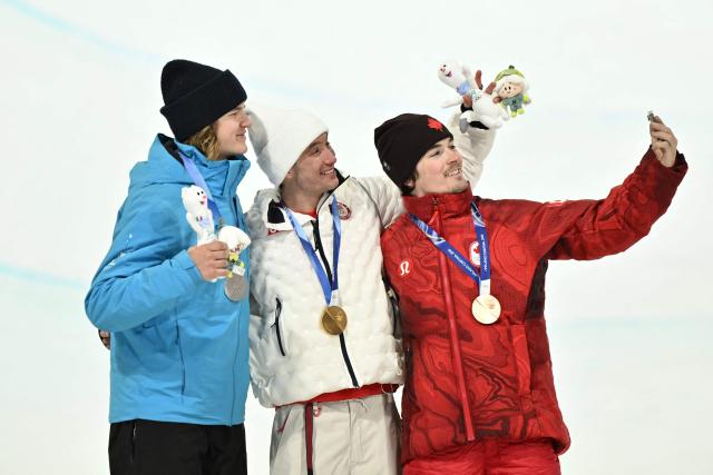 (From L) Silver medallist Estonia's Henry Sildaru, gold medallist USA's Alex Ferreira and bronze medallist Canada's Brendan Mackay pose for a selfie on the podium after the freestyle skiing men's freeski halfpipe final during the Milano Cortina 2026 Winter Olympic Games at Livigno Snow Park, in Livigno (Valtellina), on February 20, 2026. (Photo by Jeff PACHOUD / AFP)