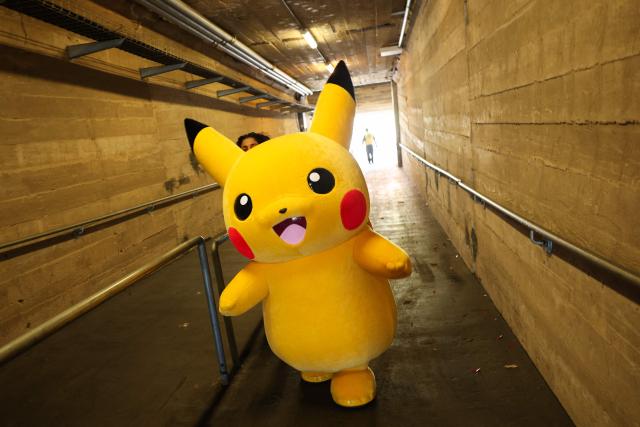 A Pikachu character walks through a tunnel after posing for pictures with fans as people play the Pokemon GO game on smartphones during the in-person Pokemon GO Tour: Kalos Los Angeles 2026 event at the Rose Bowl Stadium in Pasadena, California on February 20, 2026. Pokemon fans around the world continue to engage with the media franchise in various formats including video games, trading cards, animated series, and movies ahead of the 30th anniversary of Pokémon next week. (Photo by Patrick T. Fallon / AFP)