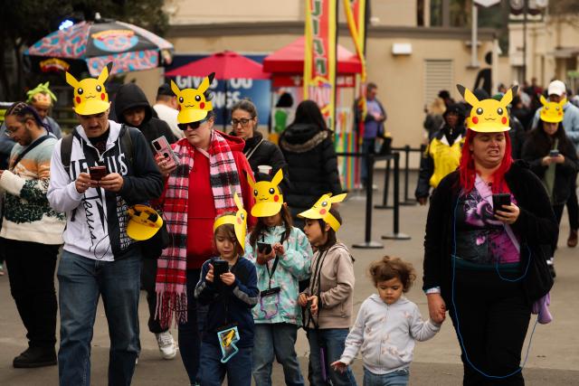 People wear Pikachu hats while playing the Pokemon GO game on smartphones during the in-person Pokemon GO Tour: Kalos Los Angeles 2026 event at the Rose Bowl Stadium in Pasadena, California on February 20, 2026. Pokemon fans around the world continue to engage with the media franchise in various formats including video games, trading cards, animated series, and movies ahead of the 30th anniversary of Pokémon next week. (Photo by Patrick T. Fallon / AFP)