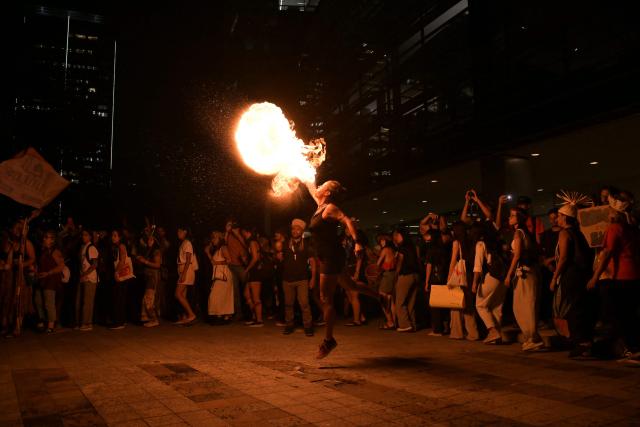 A woman performs by spitting fire during a demonstration by protesters from the Guarani ethnic group and environmental activists against dredging in the Amazon outside the headquarters of US agribusiness giant Cargill in Sao Paulo, Brazil, on February 20, 2026. (Photo by NELSON ALMEIDA / AFP)