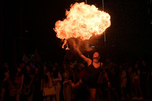 TOPSHOT - A woman performs by spitting fire during a demonstration by protesters from the Guarani ethnic group and environmental activists against dredging in the Amazon outside the headquarters of US agribusiness giant Cargill in Sao Paulo, Brazil, on February 20, 2026. (Photo by NELSON ALMEIDA / AFP)