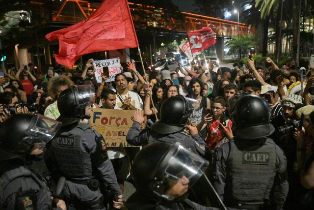 Military Police officers guard the area during a protest by Brazilian natives from the Guarani ethnic group and environmental activists against dredging in the Amazon outside the headquarters of US agribusiness giant Cargill in Sao Paulo, Brazil, on February 20, 2026. (Photo by NELSON ALMEIDA / AFP)