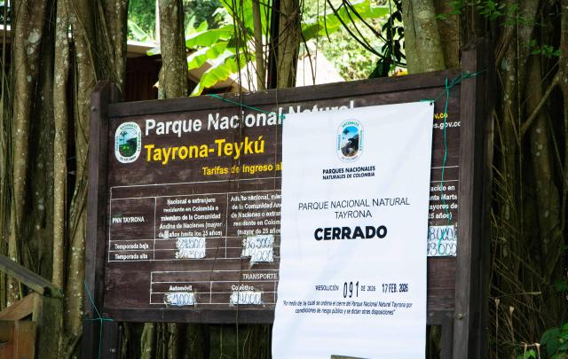 This general view shows the entrance of Tayrona National Park with banners reading ‘Closed’ in the municipality of Santa Marta, Magdalena department, Colombia, on February 20, 2026. Defense Minister Pedro Sanchez said that extortion and pressure from ‘Los Pachenca’, a paramilitary group also known as the Conquistador Self-Defense Forces of the Sierra Nevada, forced the temporary closure of the park. (Photo by Randy Montenegro / AFP)