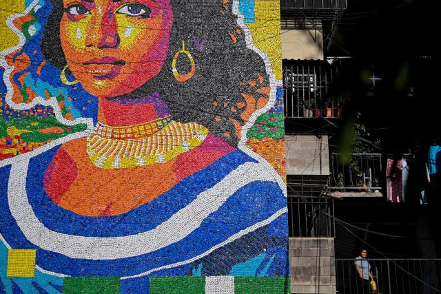 A mural made with plastic bottle caps by Venezuelan artist Oscar Olivares is seen on an apartment building in the Zacamil neighborhood in Mejicanos, El Salvador, on February 20, 2026. The artwork, over 13 meters tall and made with more than 100,000 recycled plastic bottle caps, is regarded as the world's tallest bottle-cap mural. The piece reinterprets the Mona Lisa with a Latin American identity and pays tribute to Salvadoran women. (Photo by Marvin RECINOS / AFP)
