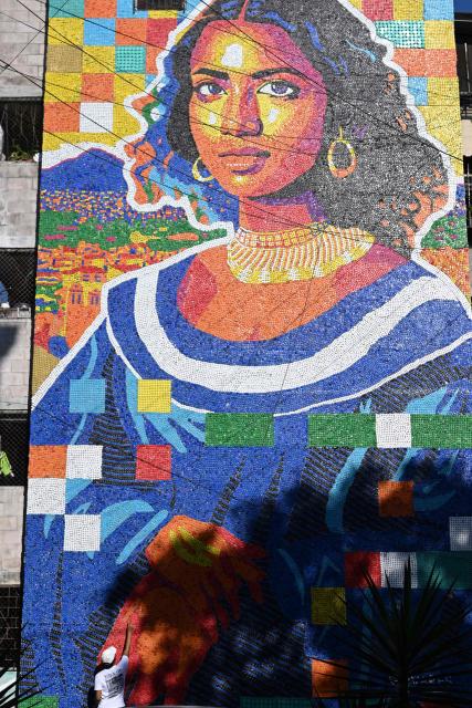 Venezuelan artist Oscar Olivares checks his mural made with plastic bottle caps on an apartment building in the Zacamil neighborhood in Mejicanos, El Salvador, on February 20, 2026. The artwork, over 13 meters tall and made with more than 100,000 recycled plastic bottle caps, is regarded as the world's tallest bottle-cap mural. The piece reinterprets the Mona Lisa with a Latin American identity and pays tribute to Salvadoran women. (Photo by Marvin RECINOS / AFP)