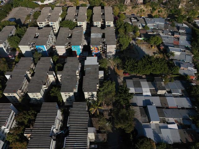 Aerial view of a mural made with plastic bottle caps by Venezuelan artist Oscar Olivares on an apartment building in the Zacamil neighborhood in Mejicanos, El Salvador, on February 20, 2026. The artwork, over 13 meters tall and made with more than 100,000 recycled plastic bottle caps, is regarded as the world's tallest bottle-cap mural. The piece reinterprets the Mona Lisa with a Latin American identity and pays tribute to Salvadoran women. (Photo by Marvin RECINOS / AFP)