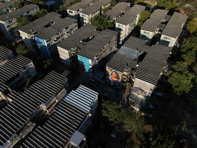 Aerial view of a mural made with plastic bottle caps by Venezuelan artist Oscar Olivares on an apartment building in the Zacamil neighborhood in Mejicanos, El Salvador, on February 20, 2026. The artwork, over 13 meters tall and made with more than 100,000 recycled plastic bottle caps, is regarded as the world's tallest bottle-cap mural. The piece reinterprets the Mona Lisa with a Latin American identity and pays tribute to Salvadoran women. (Photo by Marvin RECINOS / AFP)