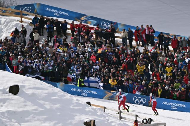 Spectators watch (From R) Norway's Emil Iversen, Norway's Johannes Hoesflot Klaebo and Norway's Martin Loewstroem Nyenget compete during the men's cross country 50km mass start final event of the Milano Cortina 2026 Winter Olympic Games at Tesero Cross-Country Skiing Stadium in Lago di Tesero (Val di Fiemme) on February 21, 2026. (Photo by Javier SORIANO / AFP)